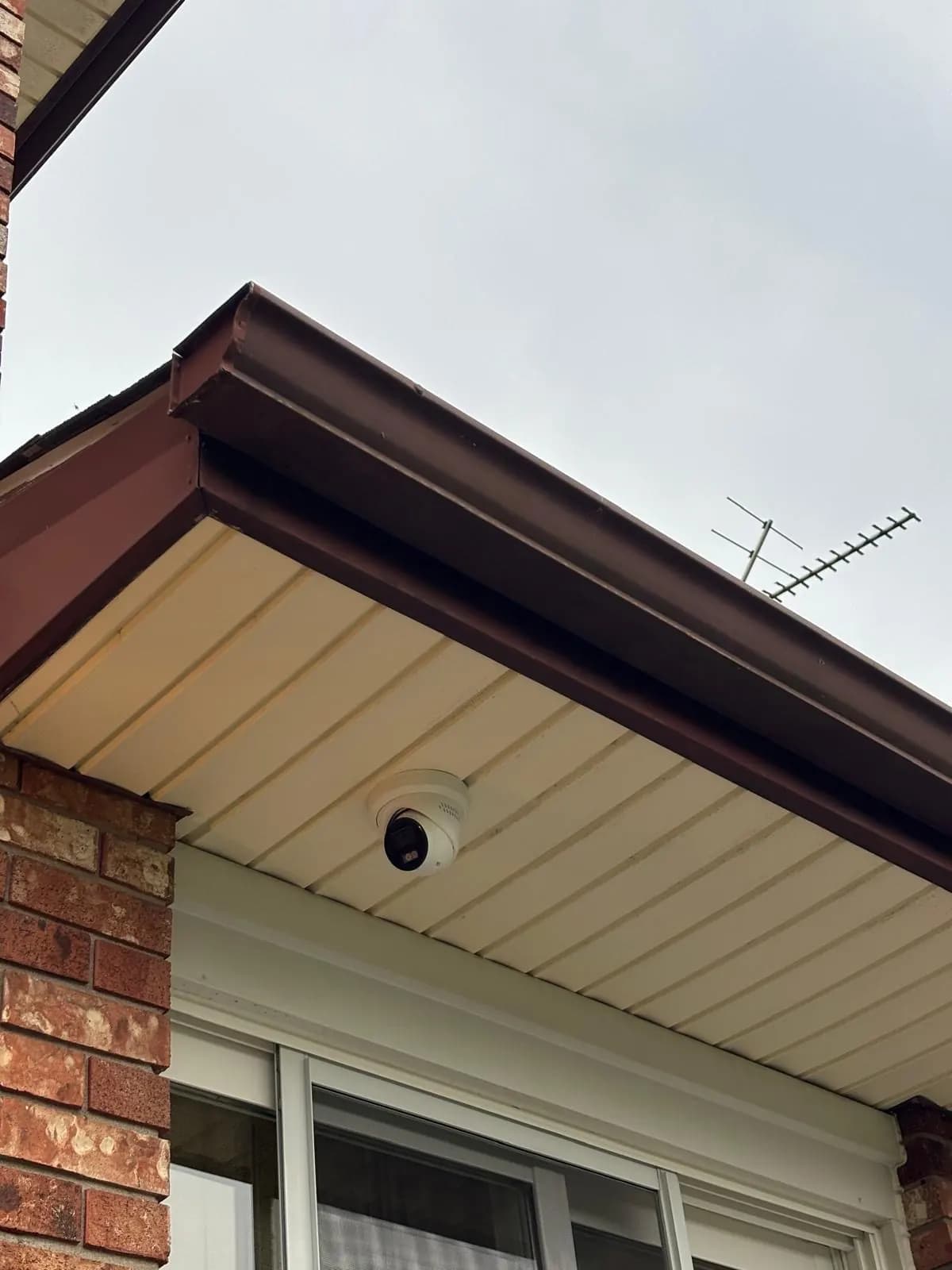 Dome camera mounted under the soffit above the front window of a house