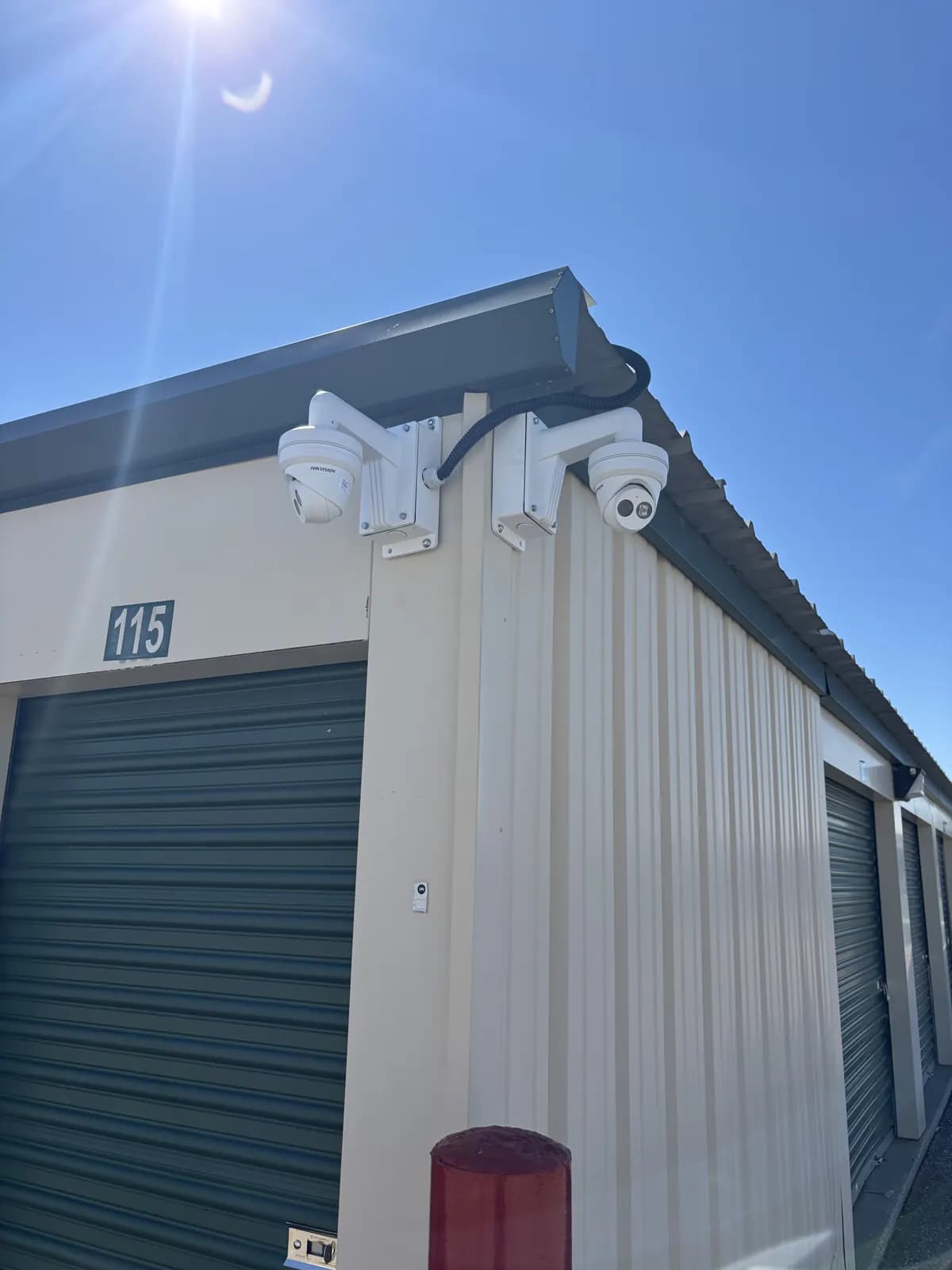 Two cameras mounted at the roofline corner of a storage unit building